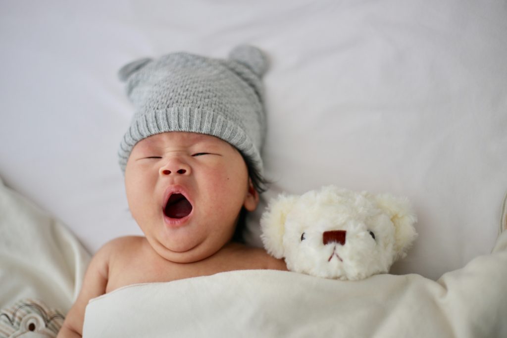 baby yawning with teddy bear and white blanket